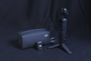 Gimbal-Kompaktkamera mit Ansteckmikrofon und Zubehör vor schwarzem Hintergrund