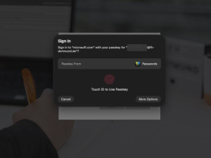 System-Dialog zur Anmeldung bei microsoft.com mittels Passkey. Die Aufforderung „Sign in to microsoft.com with your passkey“ wird angezeigt, kombiniert mit der Anweisung, die Anmeldung per Touch ID (Fingerabdrucksensor) zu bestätigen.